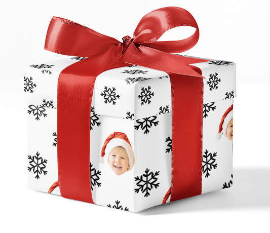 A gift box wrapped with custom wrapping paper featuring a black and white snowflake pattern, tied with a red ribbon.