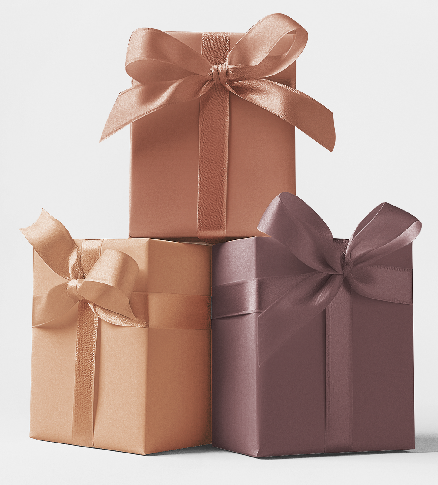 Three gift boxes wrapped in different colors of wrapping paper. The top box is copper with a satin finish, the middle is peachy-gold, and the bottom is plum with a sheen.