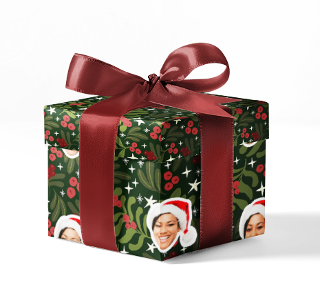 A gift box wrapped with custom wrapping paper featuring a pattern with Christmas elements and faces, tied with a red ribbon.