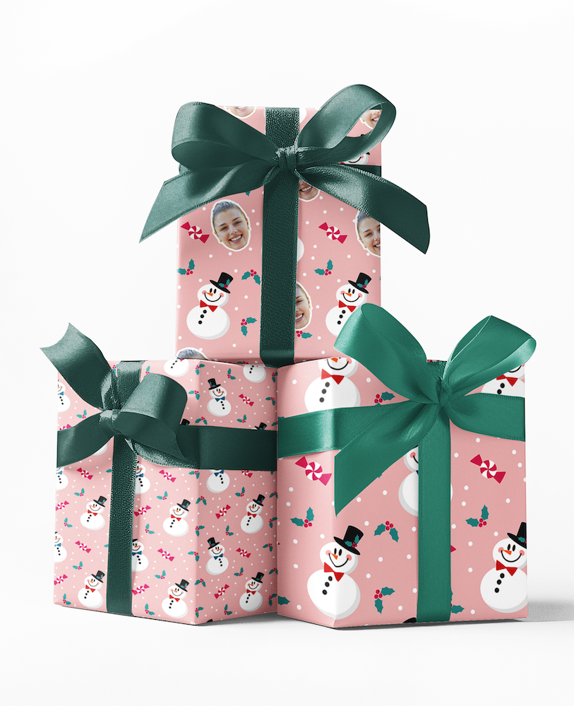 Stack of three wrapped gifts with green bows on a pink wrapping paper with a snowman pattern.