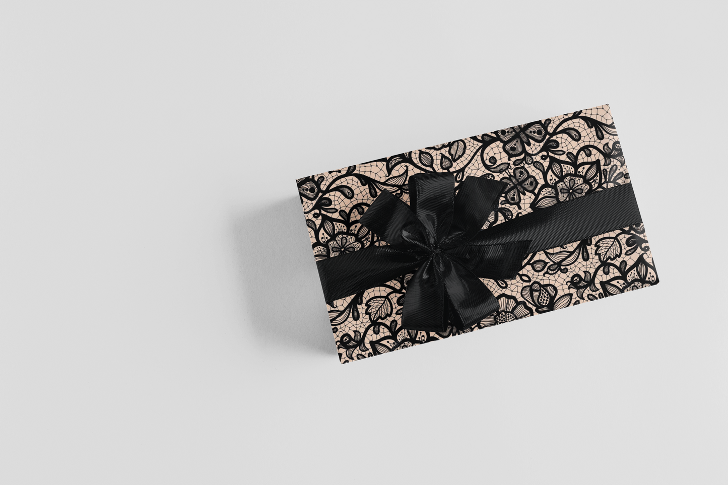 Gift box with black lace design and a black ribbon on a light gray background