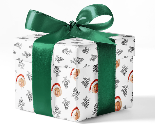 A gift box wrapped in custom wrapping paper with a pattern of pine cones and Christmas-themed decorations, tied with a green ribbon.