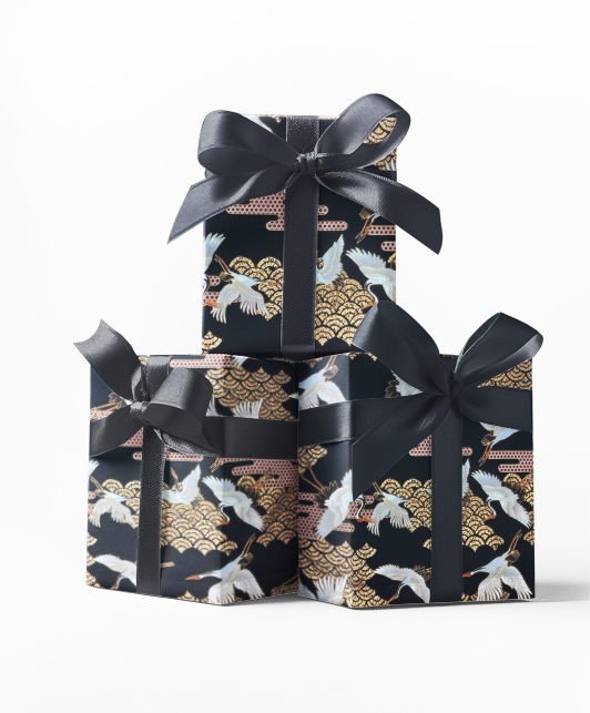 Stack of three gift boxes wrapped in black and gold patterned wrapping paper with a crane design, tied with black ribbons.
