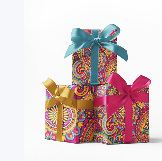 Stack of three gift boxes wrapped in custom pink paisley print wrapping paper, each box tied with different colored ribbons - blue, gold, and pink.