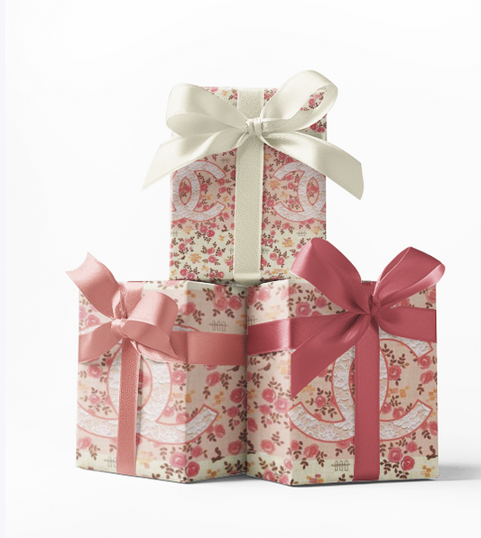 Stack of three gift boxes wrapped in custom vintage Chanel print wrapping paper, with pink and white ribbons respectively, against a white background.