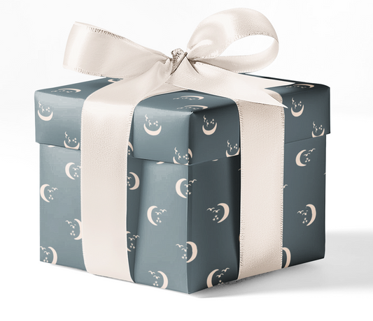 A gift box wrapped in custom wrapping paper with a pattern of moons and stars, tied with a white ribbon.