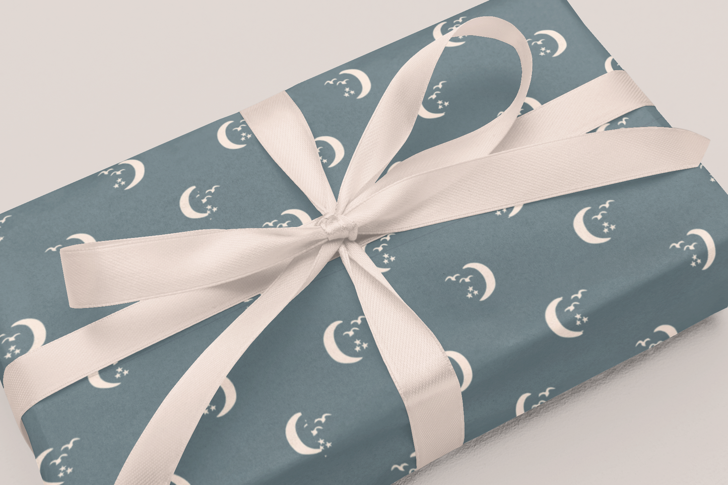 Gift wrapped in blue paper with moon patterns and a white ribbon on a light gray background