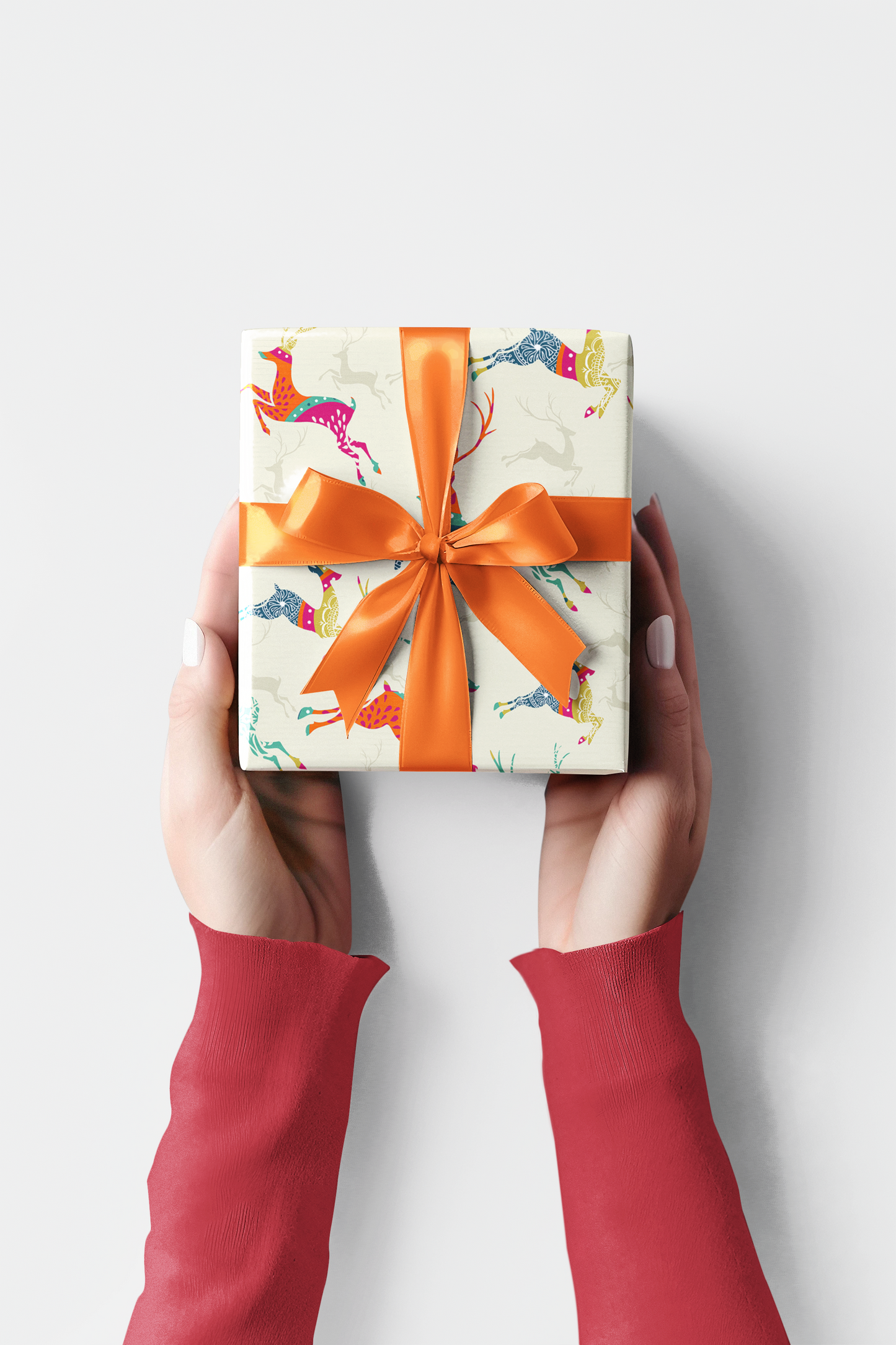 Red gift box with a bow held by hands against a pink background