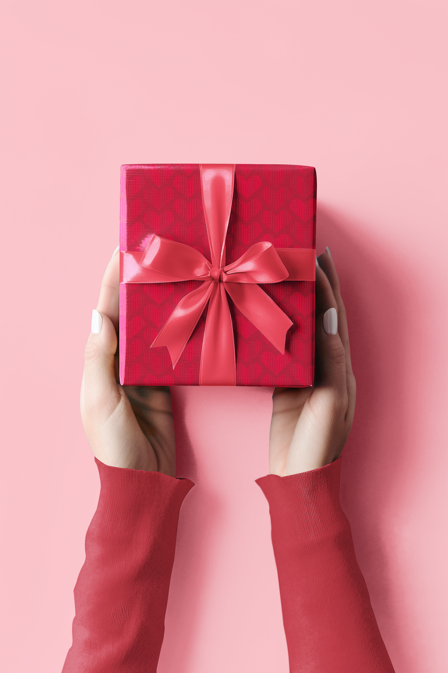 Red gift box with a bow held by hands against a pink background